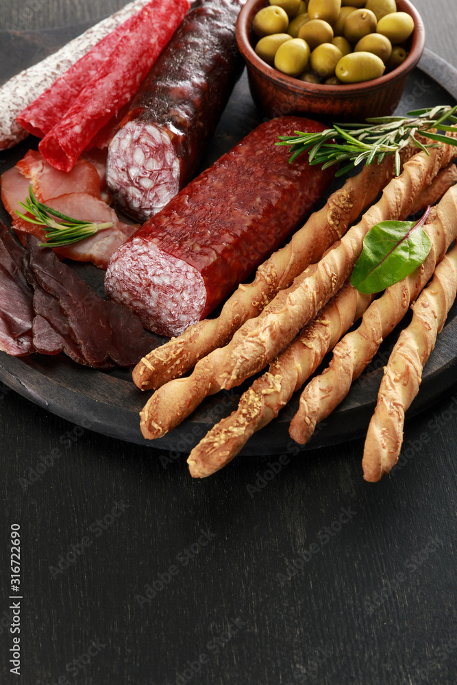 tasty meat platter served with olives and grissini on board on black surface