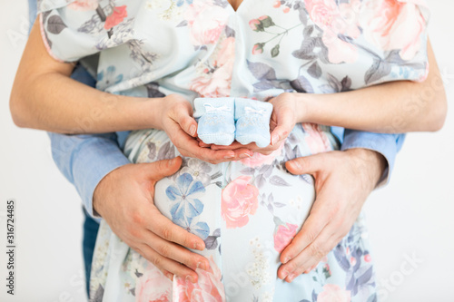 Young pregnant woman holds baby booties in front of her belly - Gender Reveal