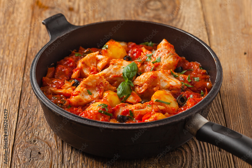 Traditionally prepared cod in Spanish. Served in tomato sauce with boiled potatoes, olivki and basil. Front view. Traditionally prepared cod in Spanish. Served in tomato sauce with boiled potatoes, olivki and basil. Front view.