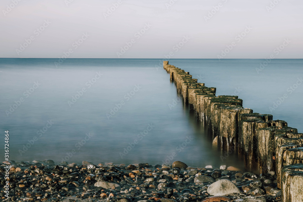 stony beach with old wooden Pier at the baltic sea on a beautiful day with blue sky - long exposure stony beach with old wooden Pier at the baltic sea on a beautiful day with blue sky - long exposure
