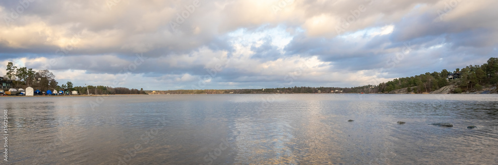 Panoramic view of Baltic Sea bay in spring. Landscape with beautiful clouds reflect on water. Horizon, skyline. Islands with pines and houses. Archipelago, Sweden. Header. 