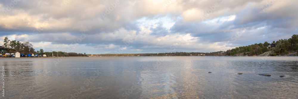 Panoramic view of Baltic Sea bay in spring. Landscape with beautiful clouds reflect on water. Horizon, skyline. Islands with pines and houses. Archipelago, Sweden. Header. Panoramic view of Baltic Sea bay in spring. Landscape with beautiful clouds reflect on water. Horizon, skyline. Islands with pines and houses. Archipelago, Sweden. Header.