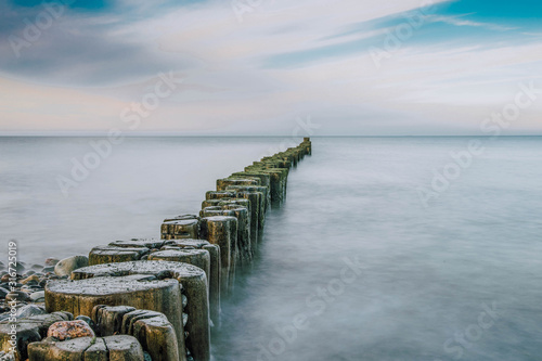 stony beach with old wooden Pier at the baltic sea on a beautiful day with blue sky - long exposure 