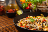 Wheat noodles with black sesame, fried in a wok with chicken and vegetables. Front view.