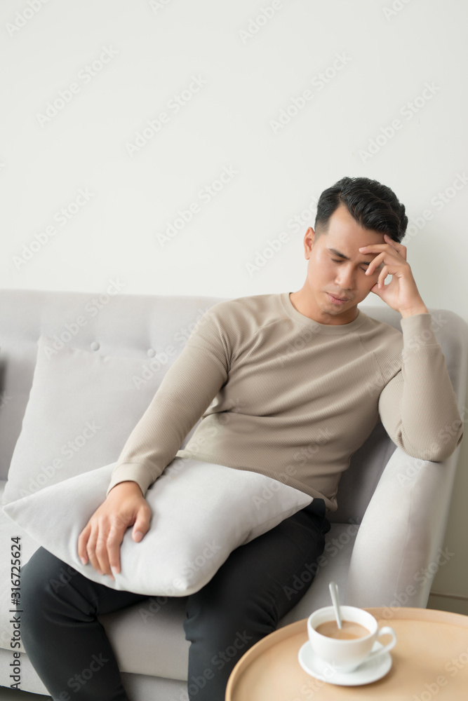 Young man suffering from headache after hard working day, sitting on couch at home, copy space Young man suffering from headache after hard working day, sitting on couch at home, copy space