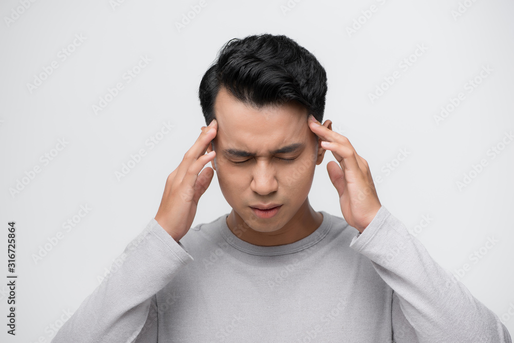 Young asian man standing over isolated white background with hand on head for pain in head because stress. Suffering migraine. Young asian man standing over isolated white background with hand on head for pain in head because stress. Suffering migraine.
