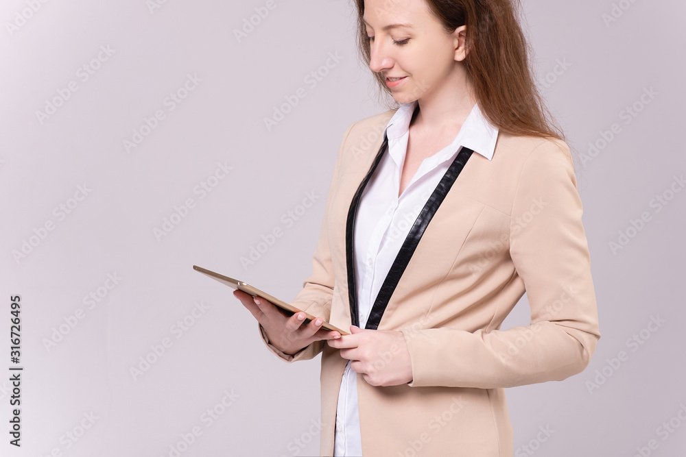 Elegant serious businesswoman in formal clothes is watching informal correspondence on a tablet and responding with a message posing on a gray background. Advertising space Elegant serious businesswoman in formal clothes is watching informal correspondence on a tablet and responding with a message posing on a gray background. Advertising space