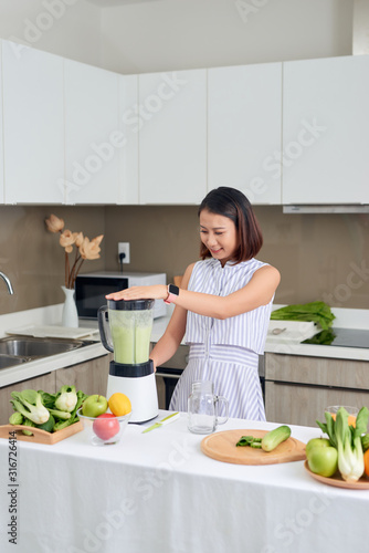 Smiling vegan Asian woman making a smoothie with fruit and vegetable in the kitchen © makistock