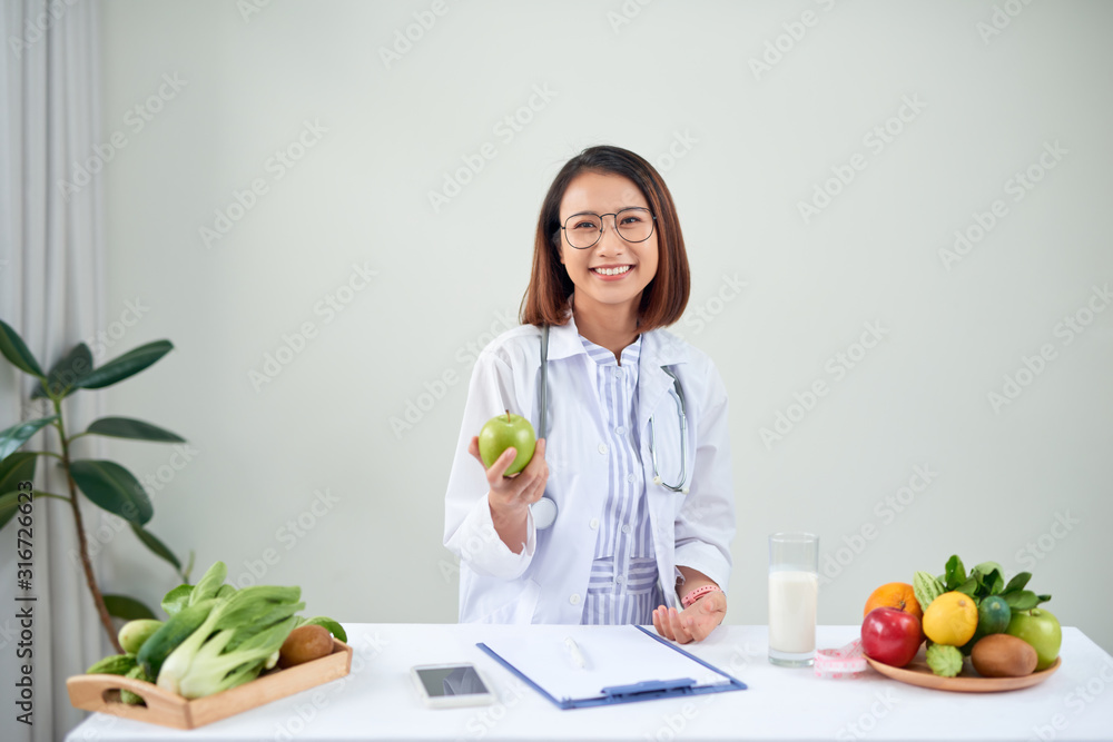 Smiling nutritionist in her office, she is showing healthy vegetables and fruits, healthcare and diet concept. Smiling nutritionist in her office, she is showing healthy vegetables and fruits, healthcare and diet concept.