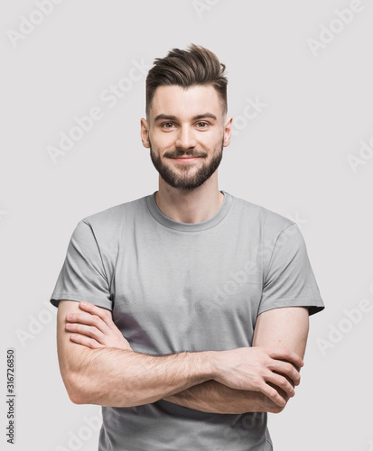 Portrait of handsome smiling young man with folded arms. Smiling joyful cheerful men with crossed hands studio shot. Isolated on gray background