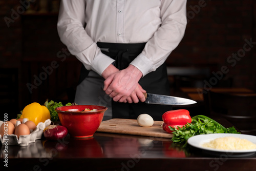 A cook with a knife stands at the table, on the table are the ingredients for breakfast.