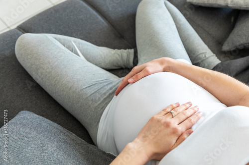 Young pregnant woman holding her belly sitting on a sofa