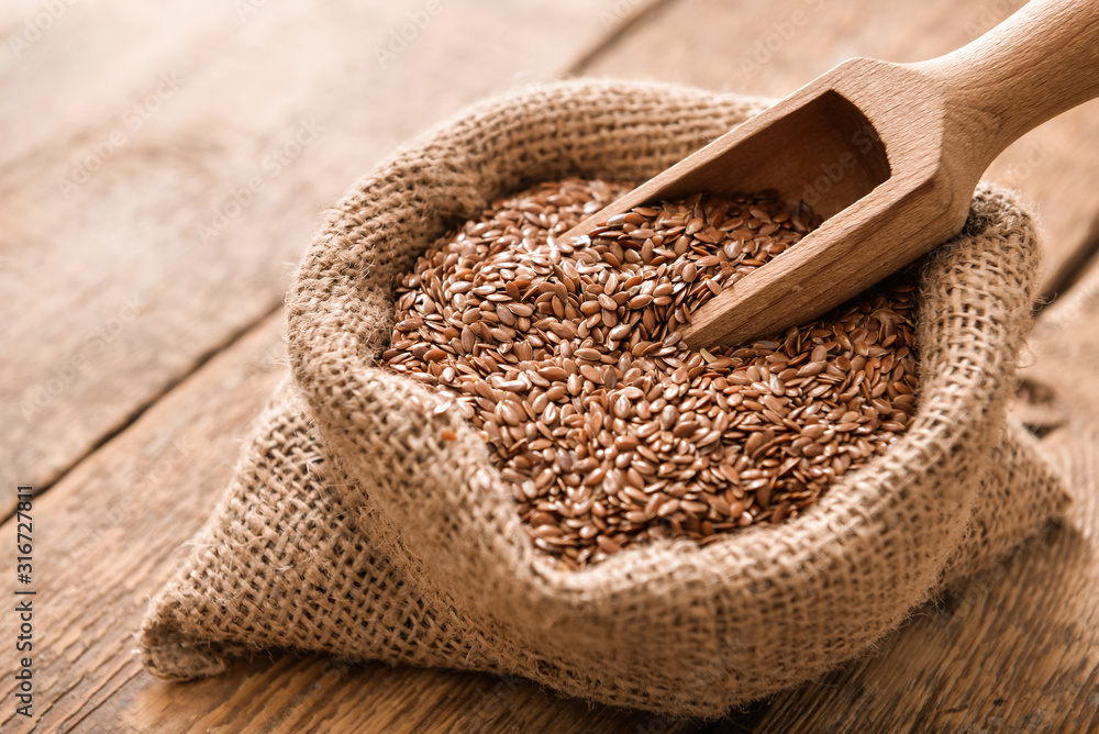 Bag with flax seeds and scoop on wooden background