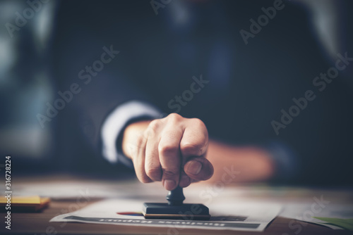 Close-up of a person's hand stamping with approved stamp on certificate document public paper at desk, notary or business people work from home, isolated for coronavirus COVID-19 protection	