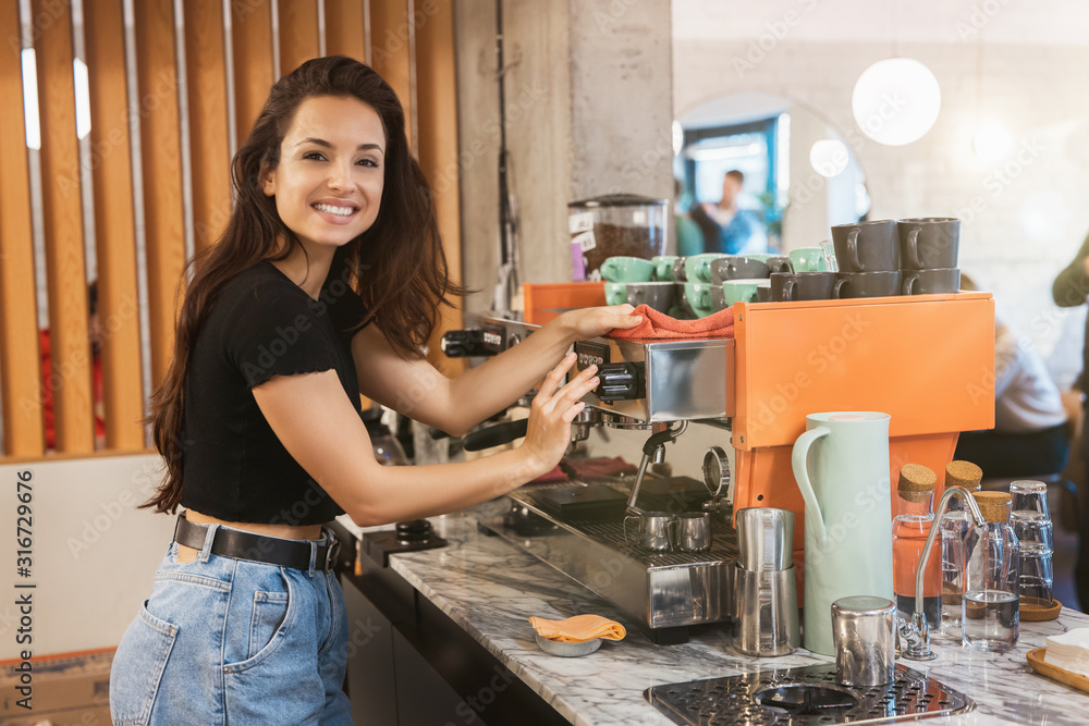young smiling barista woman cleaning professional coffee machine with dust , barist work routine