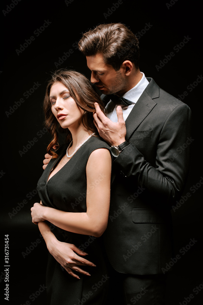handsome man in suit touching elegant woman isolated on black handsome man in suit touching elegant woman isolated on black