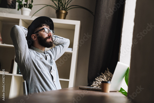 Photo of thinking young man using laptop and drinking coffee