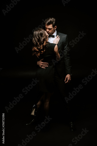 woman hugging handsome man in suit on black © LIGHTFIELD STUDIOS