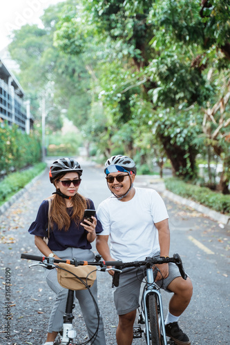 asian couple who wore helmets with cell phones seemed happy to ride bicycles together on trips in the park