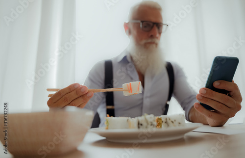 Businessman eating sushi at lunch and looking smartphone. Entrepreneur inside home studio. Job and modern concept - Image