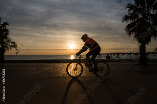 contraluz de hombre en bicicleta paseando por el paseo marítimo