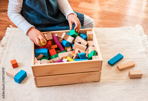 Little girl cleaning up the toy box at home. Child's space organization.