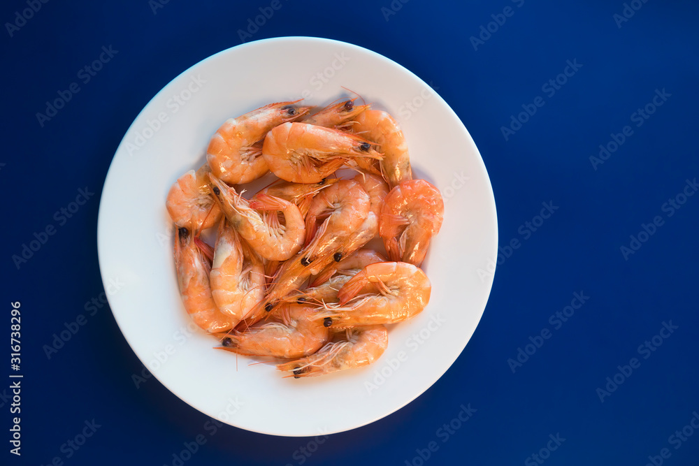 Cooked shripms, fried or boiled seafood, king tiger prawns with green herbs, spices on white plate on dark blue background. Top view. Healthy food. Carbohydrate-free keto protein diet for weight loss Cooked shripms, fried or boiled seafood, king tiger prawns with green herbs, spices on white plate on dark blue background. Top view. Healthy food. Carbohydrate-free keto protein diet for weight loss