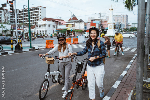 Two asian young woman wearing helmet and bags walks on the road with folding bike ready go to campus