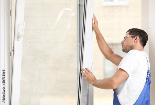 Construction worker repairing plastic window with screwdriver indoors