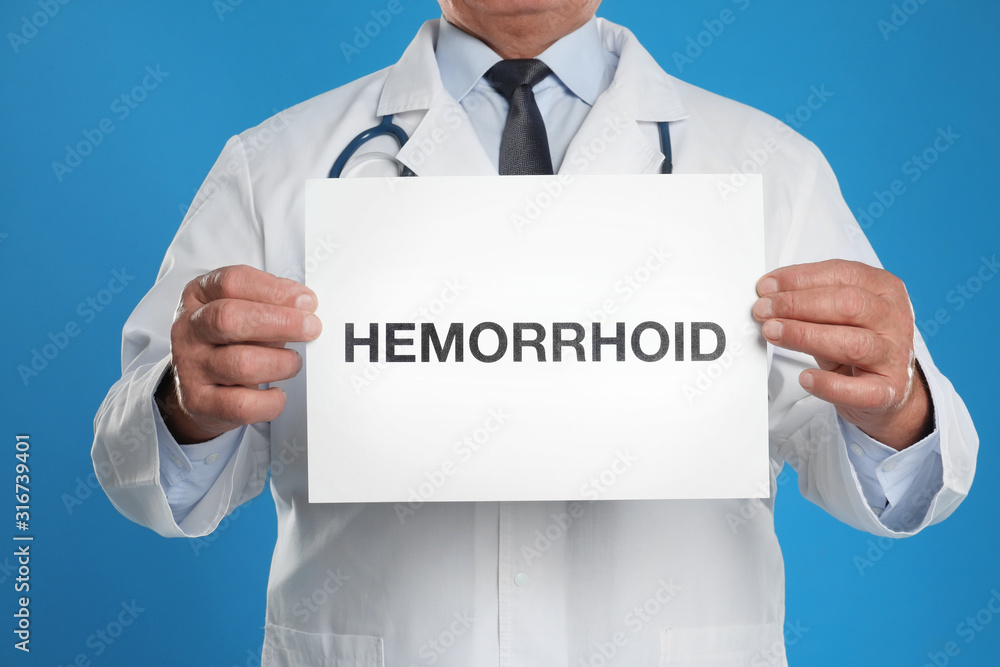 Doctor holding sign with word HEMORRHOID on blue background, closeup Doctor holding sign with word HEMORRHOID on blue background, closeup