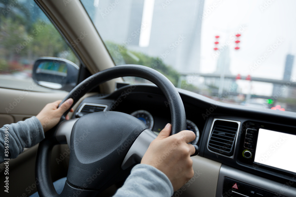 People hands holding steering wheel while driving car on city road