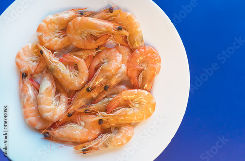 Cooked shripms, fried or boiled seafood, king tiger prawns with green herbs, spices on white plate on dark blue background. Top view. Healthy food. Carbohydrate-free keto protein diet for weight loss
