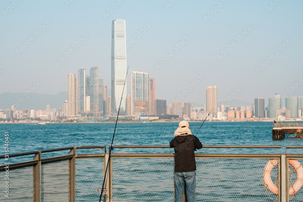 fisher man with fishing rod on coast with skyline of Hong Kong, Kowloon