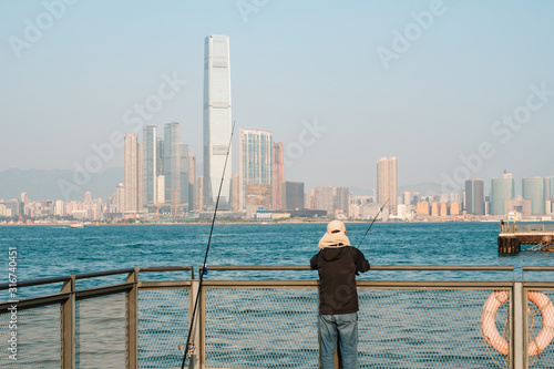 fisher man with fishing rod on coast with skyline of Hong Kong, Kowloon