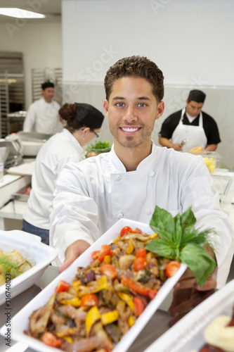 Portrait of male chef holding salad with coworkers in background