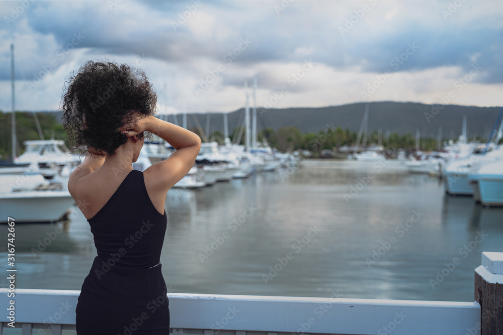 Fototapeta premium A beautiful young curly-hair woman in a little black dress is posing in the marina. Portrait Photography. Port Douglas, QLD, Australia.