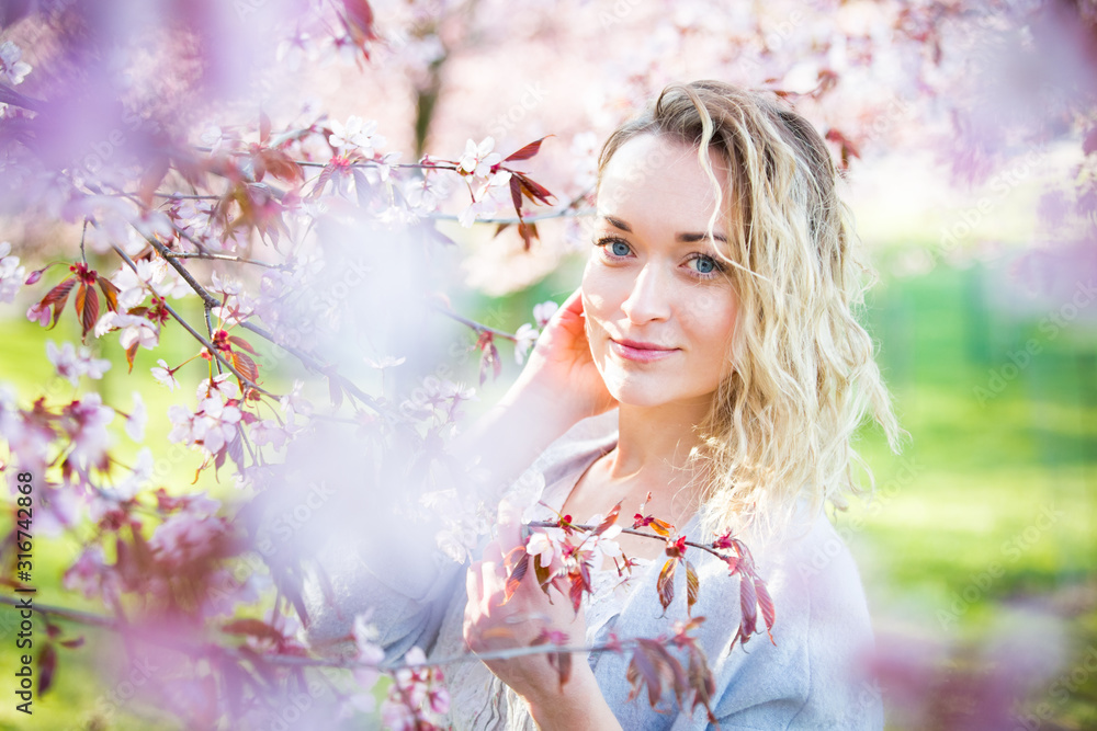 Young woman enjoying the nature in spring. Breathing fresh air and flowers aroma in beautiful park with cherry trees in bloom. Happiness concept