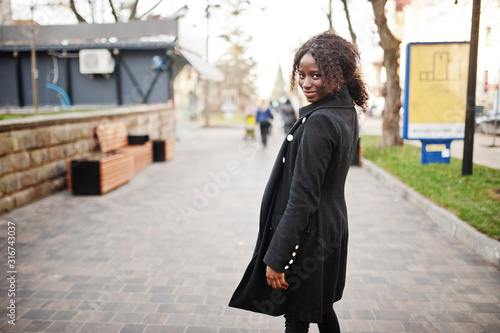 Portrait of a curly haired african woman wearing fashionable black coat and red turtleneck posing outdoor.