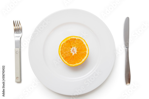 Cross section of an orange in plate with fork and knife over white background