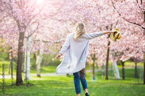 Young woman enjoying the nature in spring. Dancing, running and whirling in beautiful park with cherry trees in bloom. Happiness concept photo