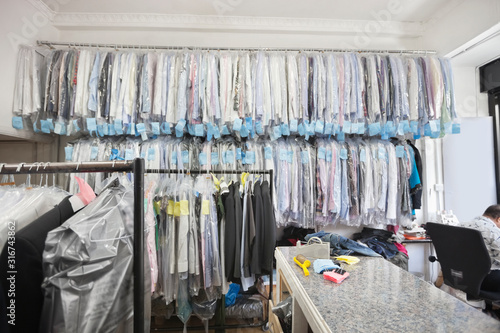 Foto Dry cleaned shirts hanging on clothes rack while tailor working in corner of the