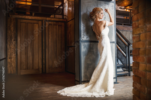 Vászonkép Beautiful blonde young woman in wedding dress in loft vintage interior stands ne