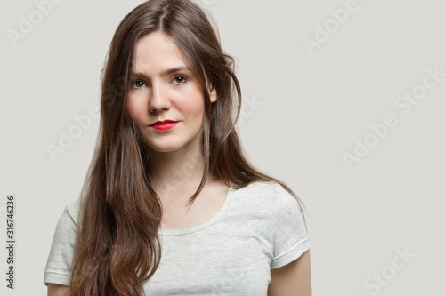 Portrait of serious young woman with red lips against gray background