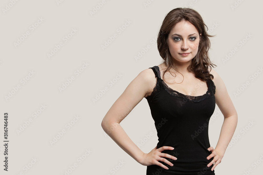 Portrait of beautiful young woman with hands on hip against gray background Portrait of beautiful young woman with hands on hip against gray background