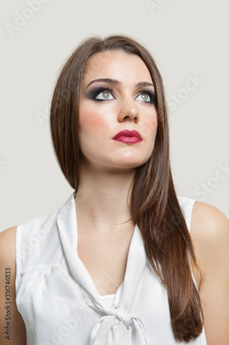 Close-up of a beautiful young woman looking up over gray background