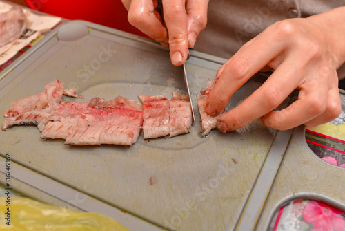 A woman cuts a herring with a knife into small pieces on a cutting board