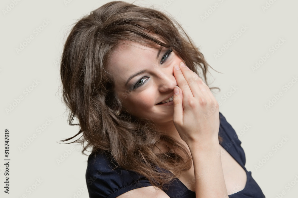 Portrait of a woman smiling with hand over mouth against gray background Portrait of a woman smiling with hand over mouth against gray background