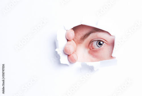 Young man peeking from ripped paper hole
