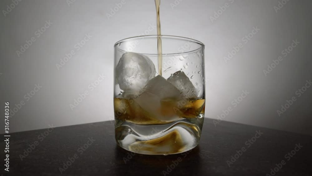 Bartender pouring aged golden whiskey into a glass with ice cubes on the table. Amber colored alcohol beverage with rocks on white background Bartender pouring aged golden whiskey into a glass with ice cubes on the table. Amber colored alcohol beverage with rocks on white background