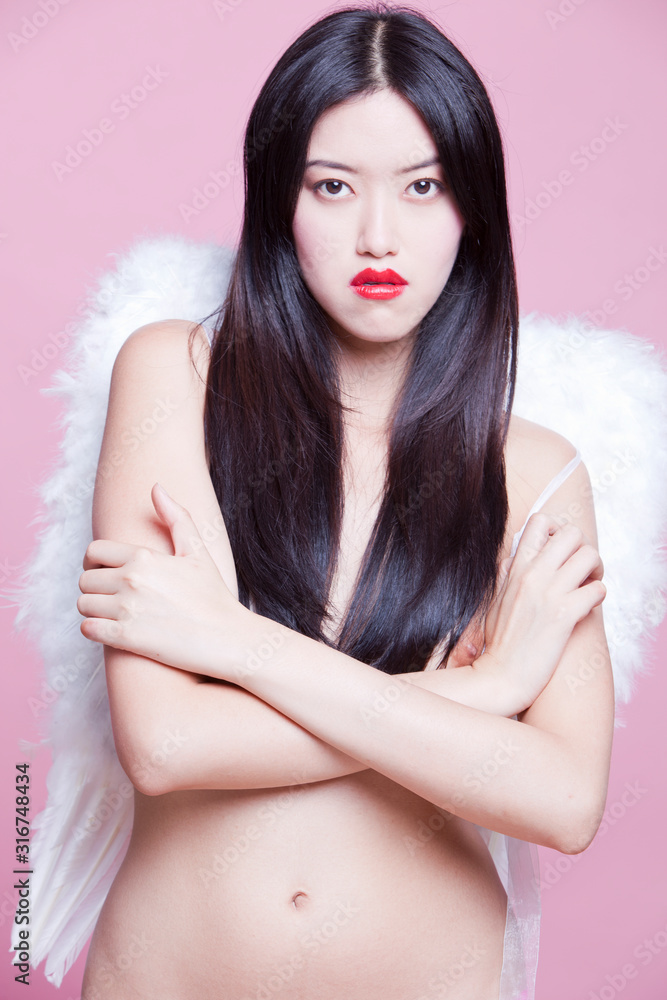 Portrait of young woman wearing angel wings against pink background